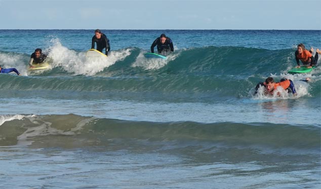 grupa początkujących surferów łapiących fale